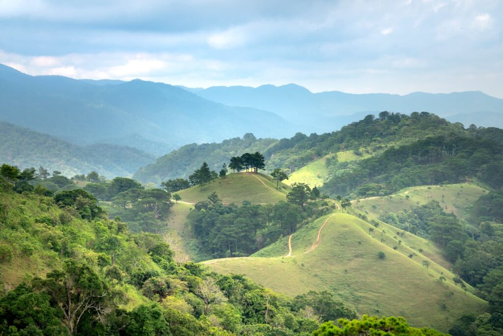 Breathtaking view of lush green hills and a majestic mountain range under a cloudy blue sky.